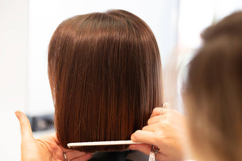 Hairdresser cutting brown hair with comb, professional salon colorist at work.