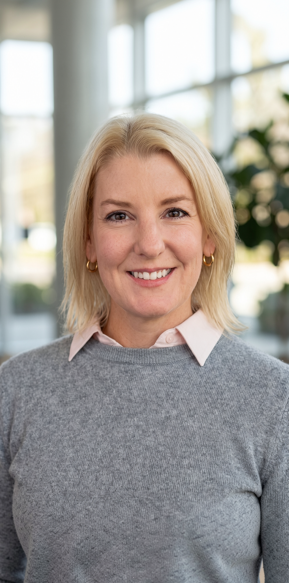 Studio portrait photography of a smiling blonde woman in professional attire. The background is softly blurred.