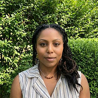 Linda Shelton, Reiki Master and licensed massage therapist, outdoors in striped top with necklace and green foliage background.