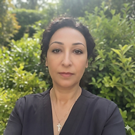 Zoey Zorica Knezevic, licensed massage therapist, standing outdoors in front of lush green foliage, wearing a dark top and cross necklace.