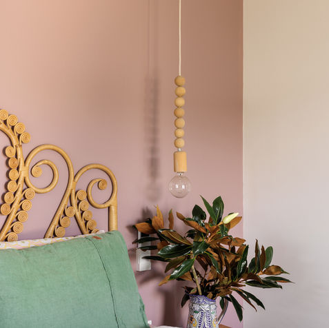 Stylish bedroom corner with woven headboard, pink wall, pendant light, plant.