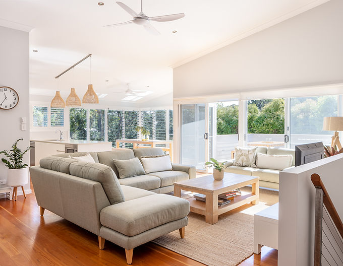 Bright open-plan living room with L-shaped sofa, wooden floors, and large windows at Ocean Escape Holiday rental accommodation Boomerang Beach NSW Australia.