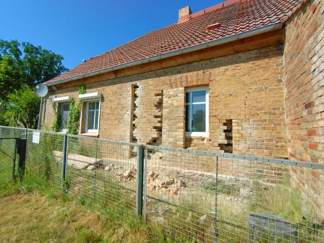 Hausansicht mit halb rausgebrochener Türöffnung und halb zugemauertem Fenster