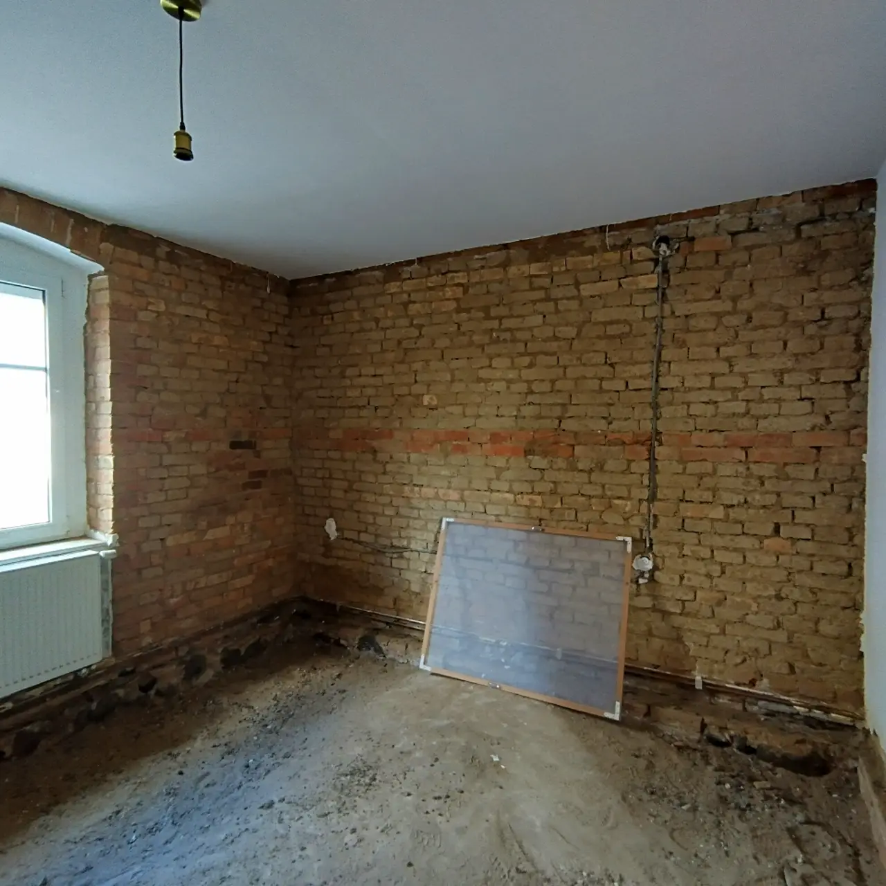 Zimmer im Rohbau mit Wandverkledung und Fußboden entfernt, sichtbare Ziegelwand