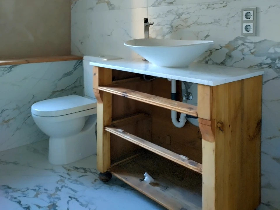 Badezimmer mit Holzkommode als Waschtisch. Im Hintergrund Toilette, Fliesen an der Wand.