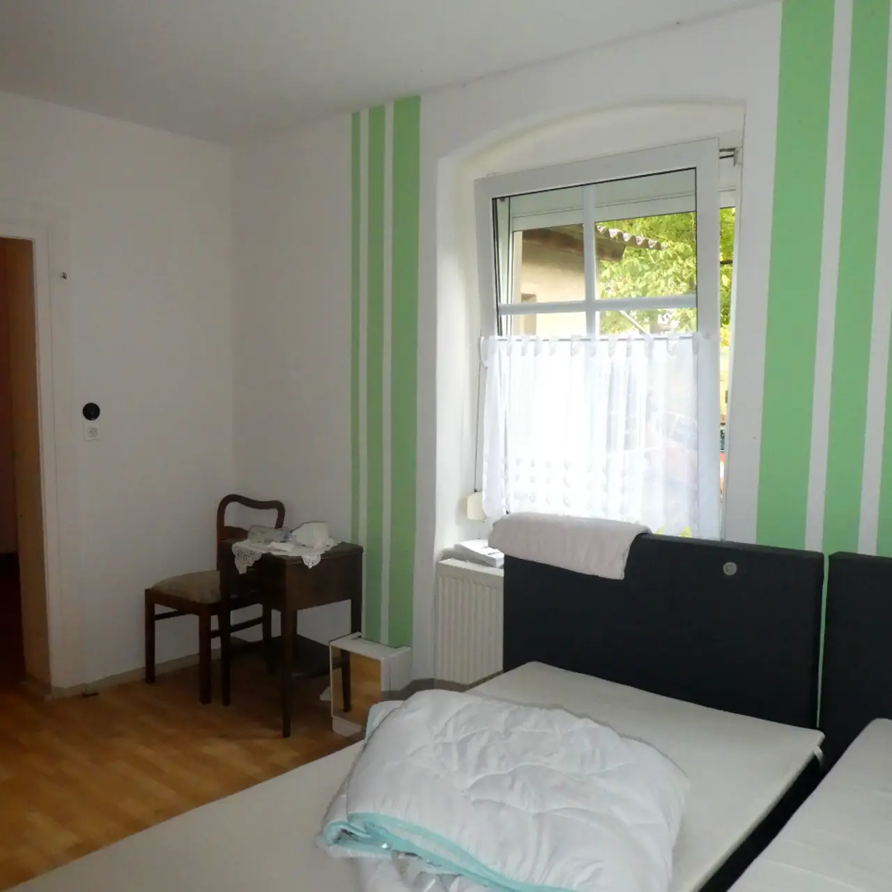 Raum mit grünen Farbakzenten an der Wand und Bettgestellen im Vordergrund