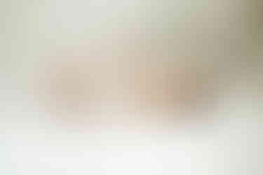 newborn wearing a crocheted onsie stretching their arms and legs lying on a white duvet