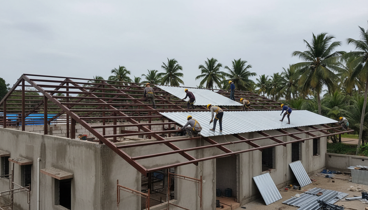 Eye-level view of workers fitting insulated roofing sheets on a low-rise building in Kerala