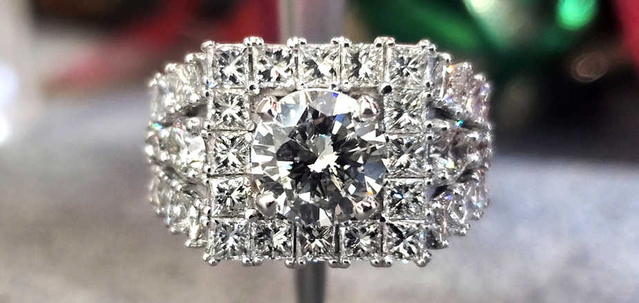 Round center diamond set in 14k white gold surrounded by a halo and rows of princess cut diamonds.