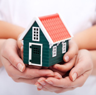 Parents holding hands with toddler while holding a model of a house