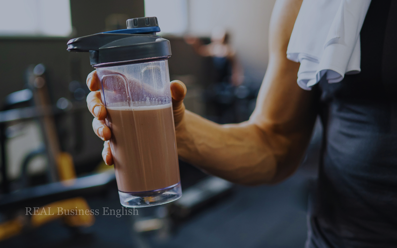 Person holding a chocolate protein shake in a gym for Business English workplace practice.