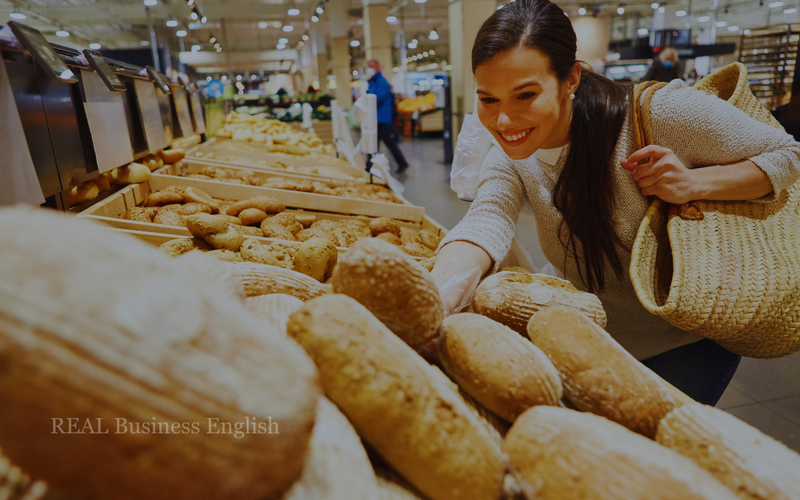 Shopper reaching for a loaf of bread in a supermarket bakery section.