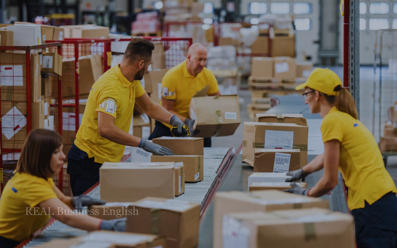 Workers packing cardboard boxes along a conveyor belt in a warehouse.