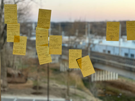 Image of yellow post-it notes filled with hand writing and stuck to a window. Background is an urban landscape with train track in the fore ground and the city of St Louis in the back ground.