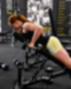 Woman performing a back extension exercise on an incline bench in a gym.