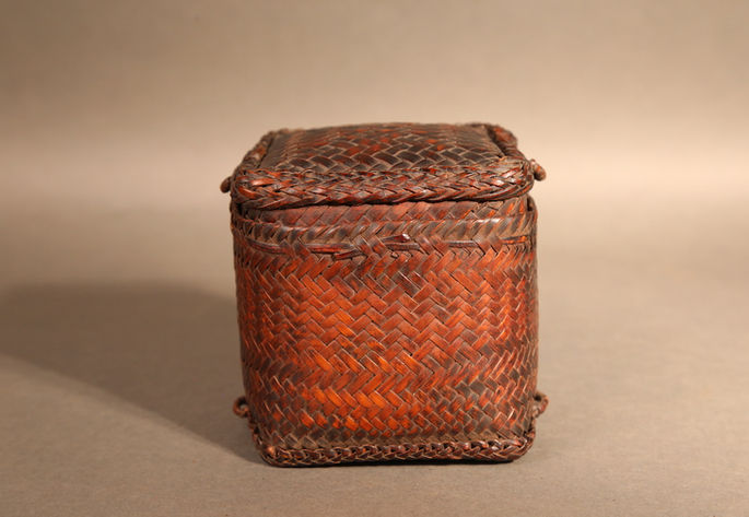 A small, square, woven bamboo split purse with a lid covering much of its body