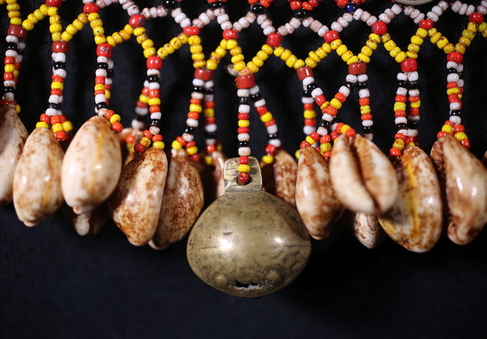 A detailed shot of the karawaweng’s brass bell and cowry shells embellishments