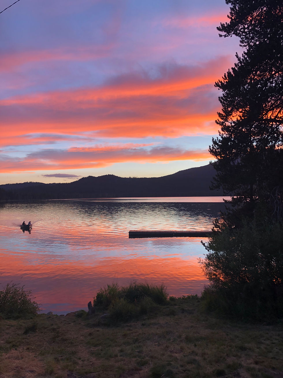 Lake with bright pink sunset sky reflecting on it and mountains silhouetted