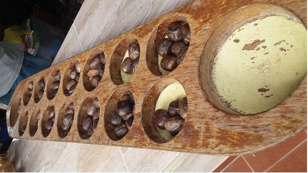 Fa társasjáték, kagylószerű bemarásokkal, tele barna magokkal. Padlón és asztalon fekszik. Színek: barna és sárgás foltok.