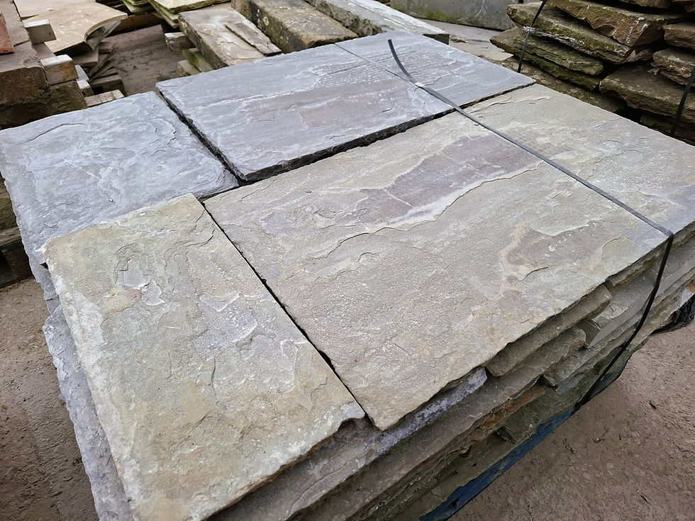 Reclaimed sandstone flagstones stacked in mixed sizes showing natural colour variation and worn edges