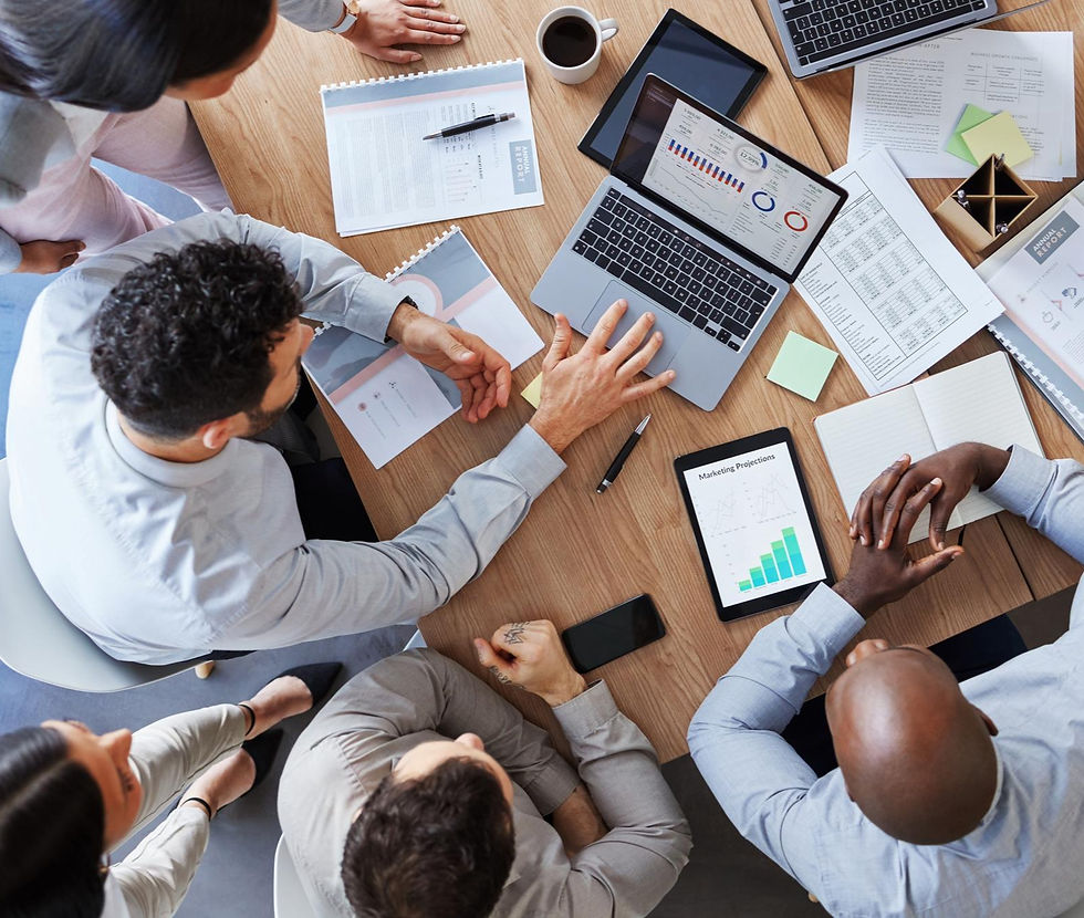 Reunião de equipe vista de cima, com laptop exibindo gráficos, relatórios, café e pessoas analisando dados numa mesa de madeira.