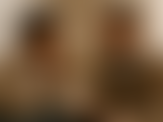 A young woman sits on a sofa in a softly lit therapy room, appearing pensive with her hands near her face. A therapist beside her listens attentively, creating a calm and empathetic atmosphere.