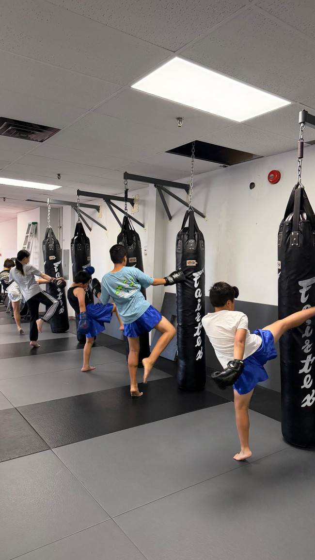 Young students practising Muay Thai kicks on heavy bags