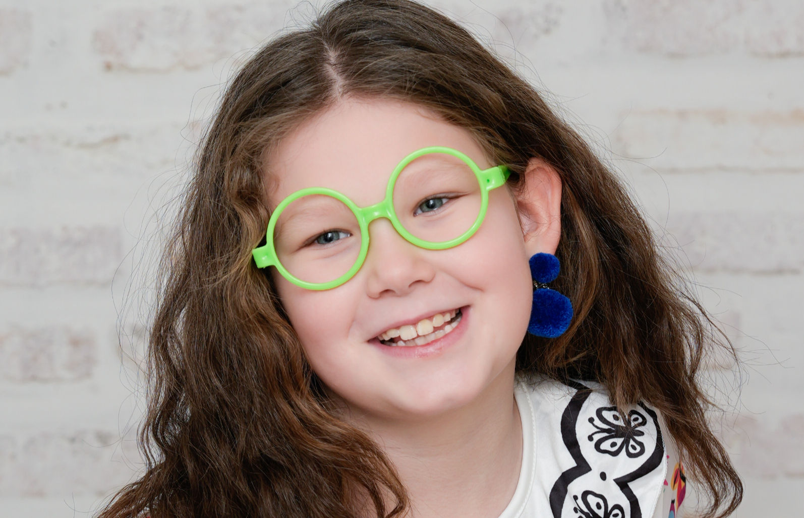 Lächelndes Mädchen mit grünen Brillen und blauen Ohrringen