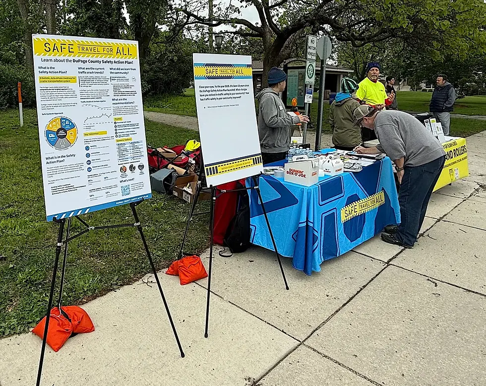 Community outreach table for DuPage County’s Safe Travel for All initiative, with display boards, flyers and residents engaging with staff. The setup includes safety plan details and a table covered in branded materials.