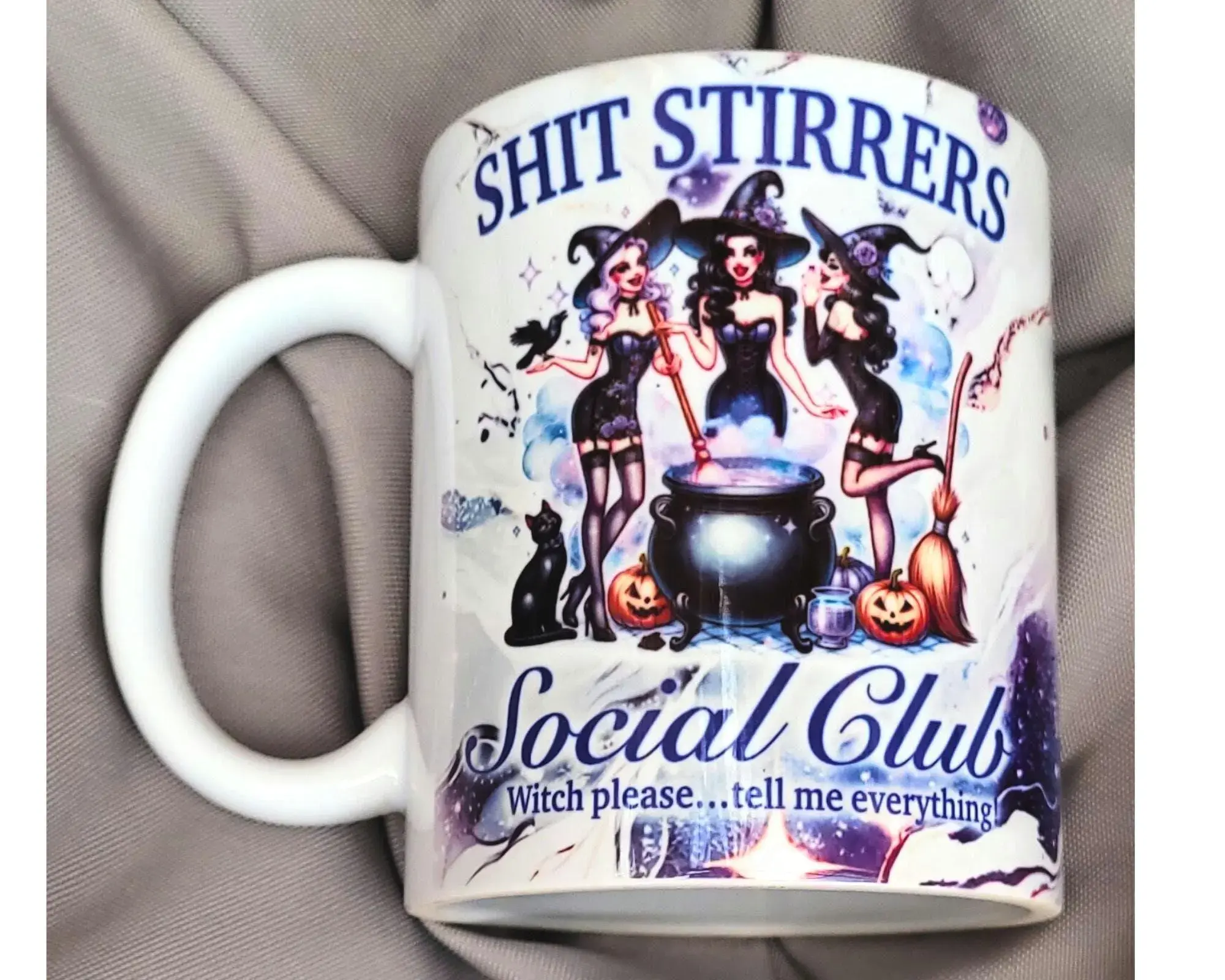 White ceramic witchy mug featuring three witches around a cauldron with the text “Shit Stirrers Social Club