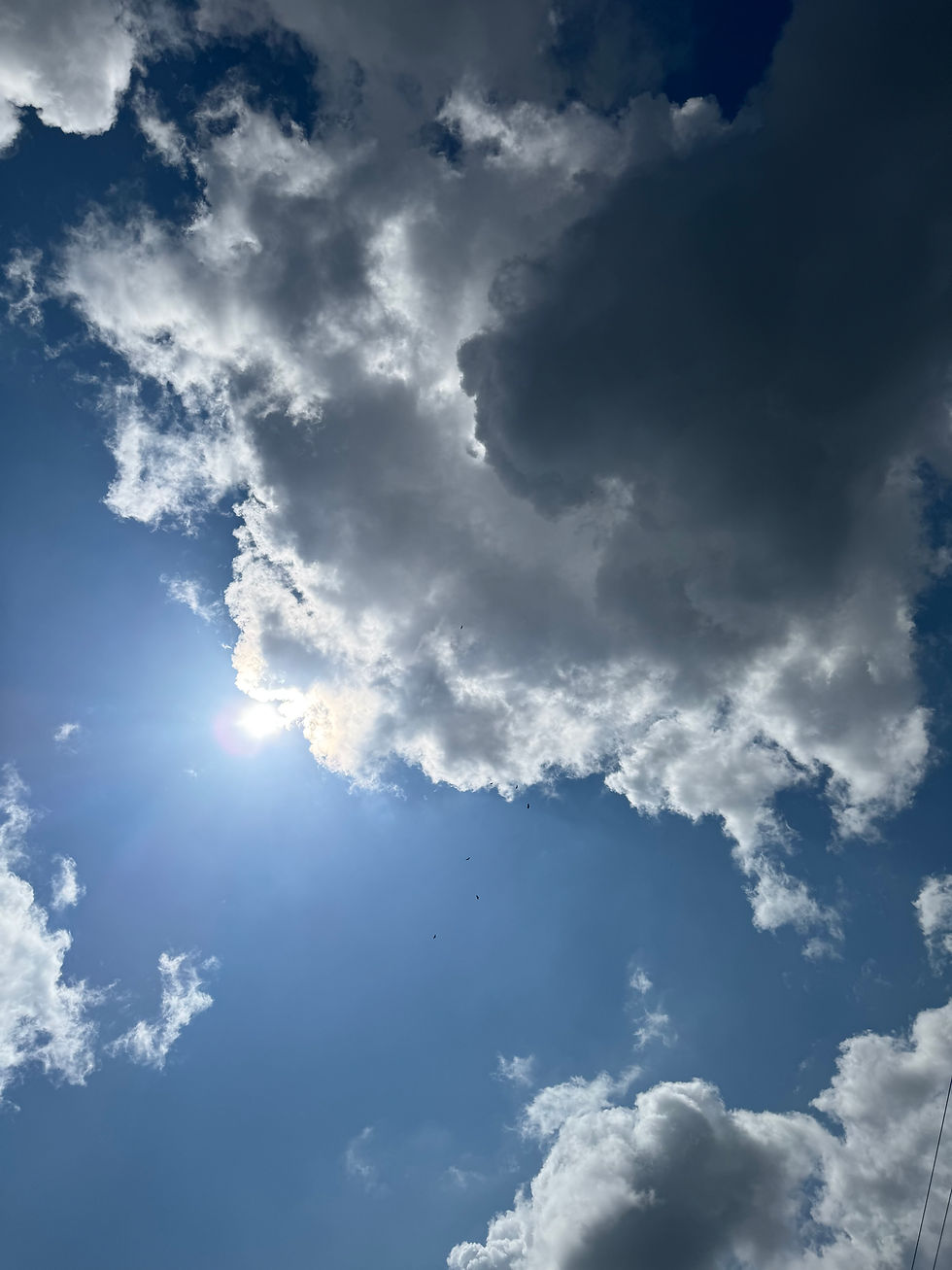 Bright sunlight shining through dramatic white clouds in a blue sky, symbolizing spiritual connection, intuition, higher awareness, peace, and inner guidance.