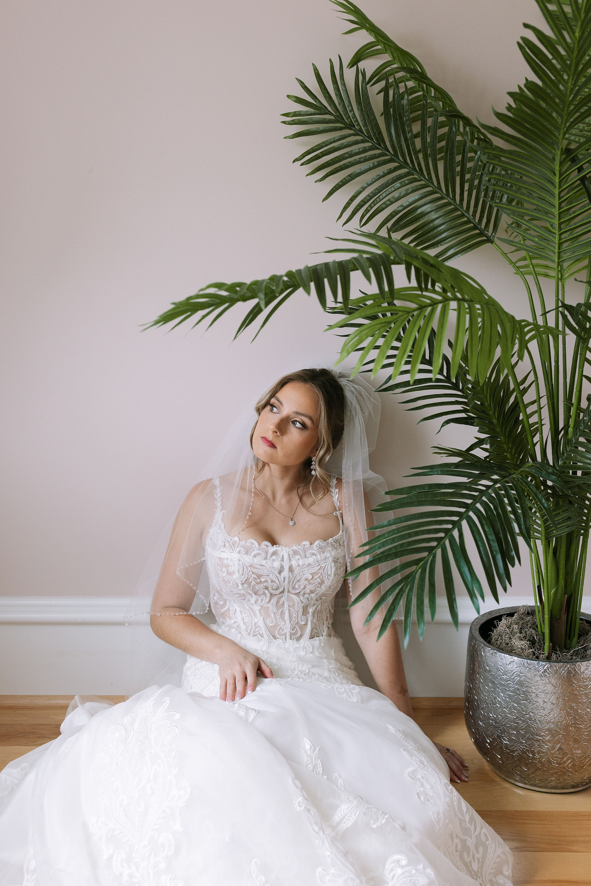 Bride sitting against a wall next to a plant