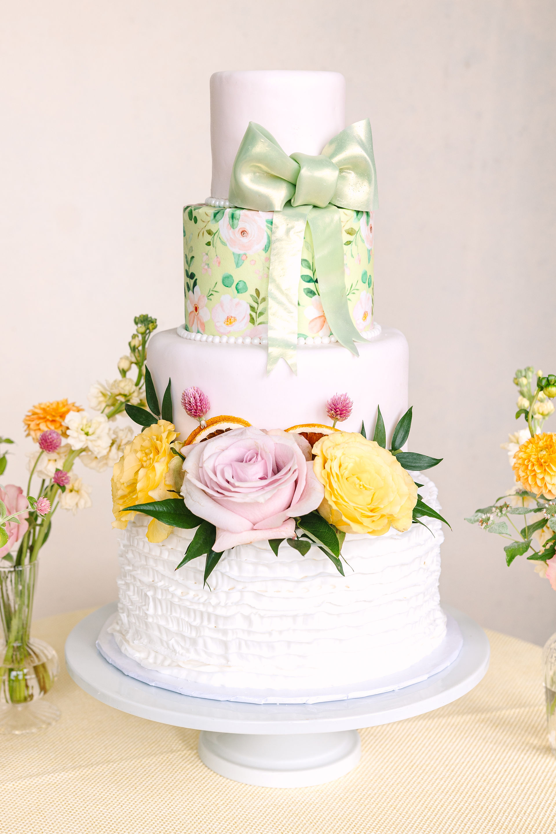 A four tiered wedding cake with flowers and a bow