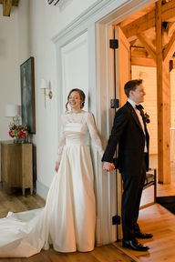 A groom and bride have a first touch holding hands on either side of door
