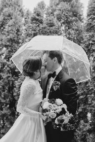 Newlyweds kiss under an umbrella outside