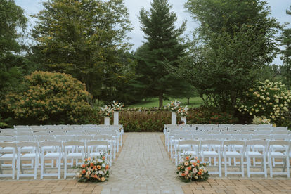 An outdoor wedding ceremony with flowers pillars and chairs