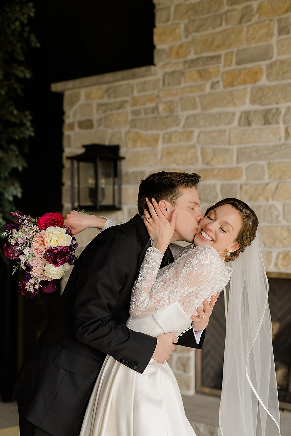 A groom kisses his bride on the cheek while she laughs