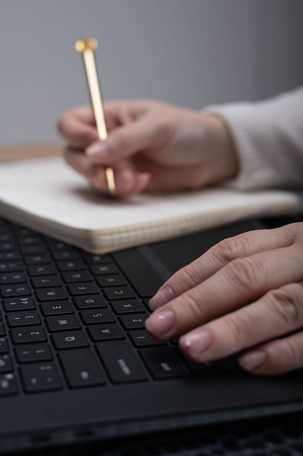 a white woman's hands holding a gold pen writing in a notebook resting on a laptop keyboard