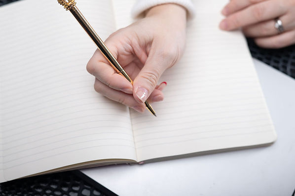a white woman's hand holding a gold pen and writing in a white lined notebook