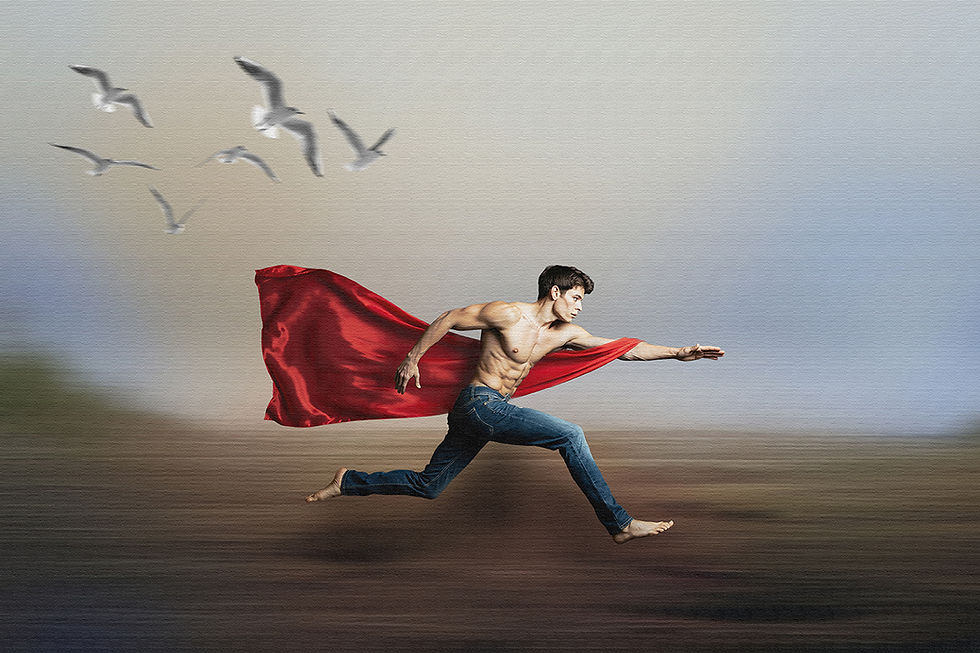 Homme torse nu courant sur une plage, capté en plein saut avec un bras tendu vers l’avant, portant un jean et une cape rouge flottant au vent derrière lui; fond flou avec horizon marin et quelques oiseaux dans le ciel.