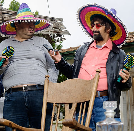 השחקן אסי ישראלוף ושחקן נוסף עומדים, הם חובשים כובעי סומבררו ומחזיקים רעשנים וטלפון נייד