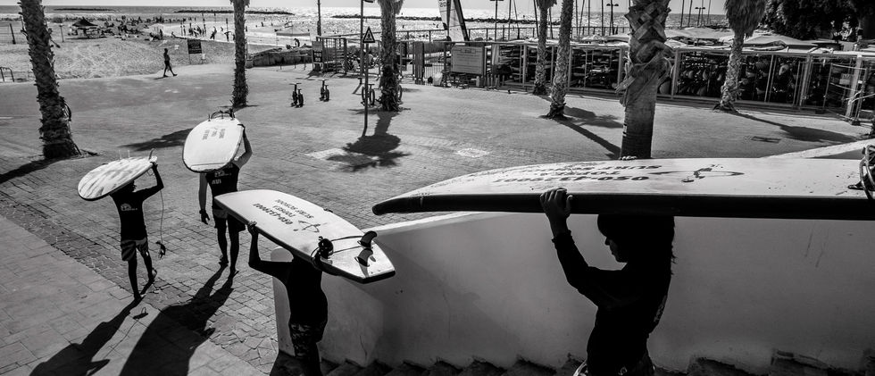 ארבעה צעירים יורדים במדרגות בדרך לים כשעל ראשם גלשנים – הצילום בוצע בשחור לבן