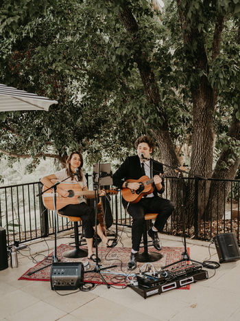 Acoustic duo Adam & Jasmin play guitar and sing harmonies during an outdoor cocktail hour at a wedding in the Brisbane