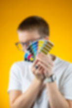 Antonia Buchmann hält einen Farbfächer vor ihr Gesicht, welches einen Einblick in das Farbmanagement und die Designexpertise bei toniplustobi.com bietet.