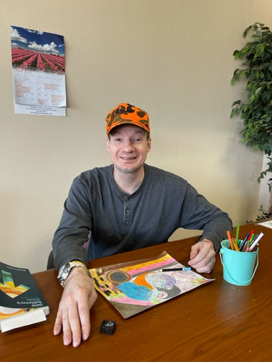 Man sitting at a table with a painting and painting supplies in front of him.