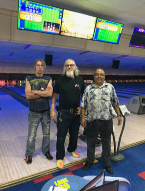 Group of men at a bowling alley with purple lights in the background.