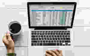cup of coffee next to laptop showing data charts and graphs