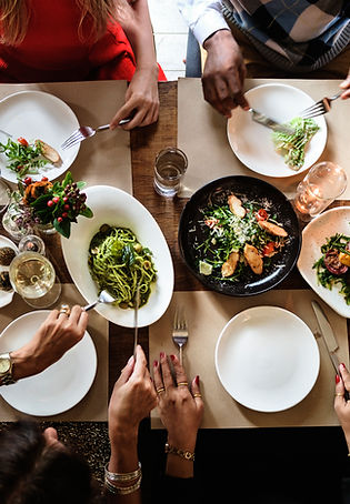 Overhead view of a group enjoying a gourmet meal with fresh salads, pasta, and fine wine, showcasing private chef dining expe