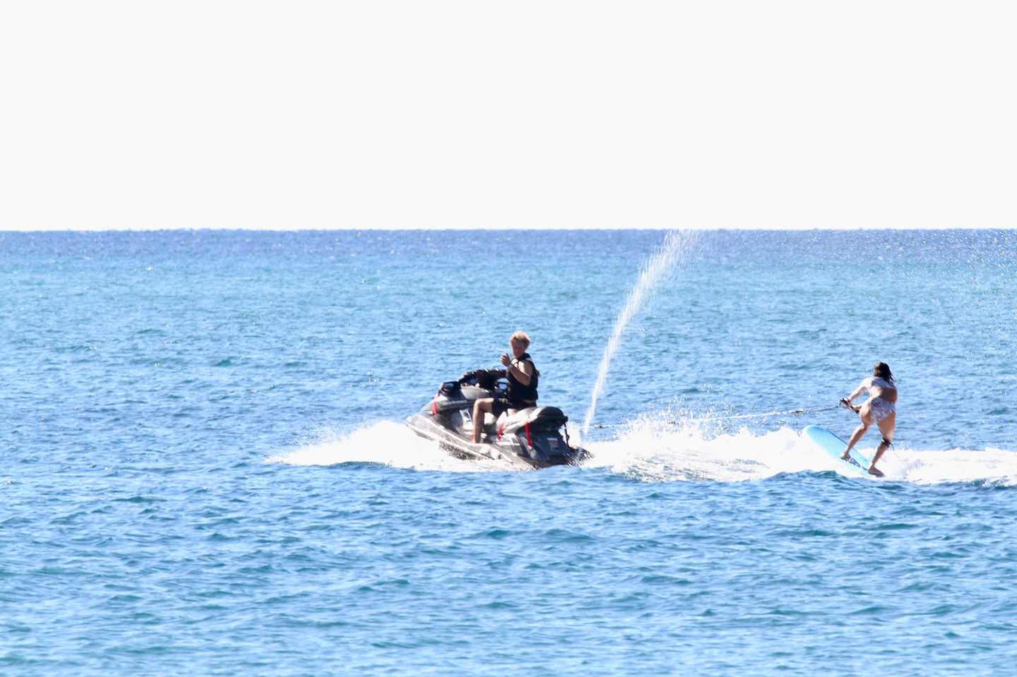 Woman wakesurfing behind a jet ski on a sunny ocean