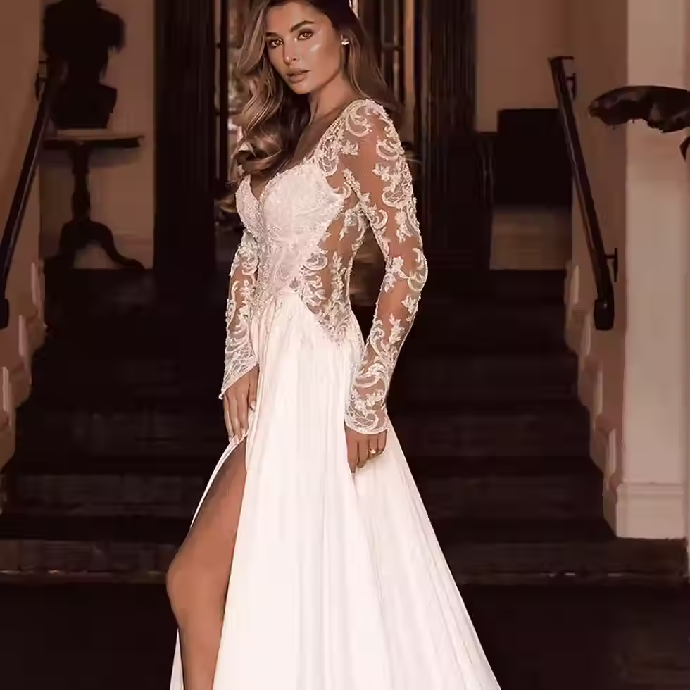 A woman wearing a long-sleeved white dress with lace details and a high slit, standing elegantly on stair steps.